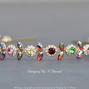 May include: A gold headband with a row of colorful iridescent rhinestones. The rhinestones are set in a floral design with small clear rhinestones surrounding each larger colored rhinestone.