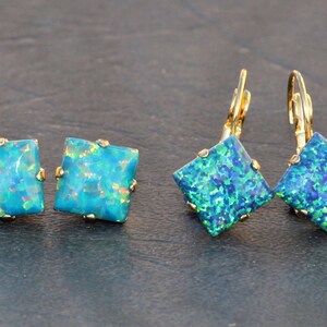 May include: Two pairs of earrings with square, iridescent blue-green opal stones. One pair is stud earrings, and the other is lever-back earrings. The gold-colored settings add a touch of elegance to the jewelry.
