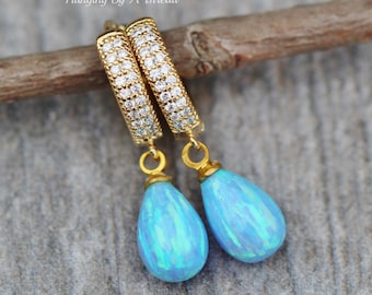 May include: Gold hoop earrings with a row of clear cubic zirconia stones and a dangling teardrop shaped blue opal.