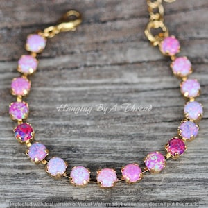 May include: A gold chain bracelet with a gradient of pink, white, and purple opal stones. The bracelet is on a wooden surface.