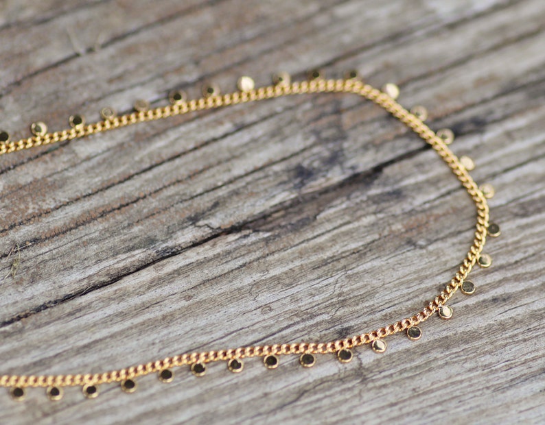Puede incluir: Un collar de cadena de oro con peque&ntilde;os colgantes redondos. El collar est&aacute; sobre una superficie de madera.