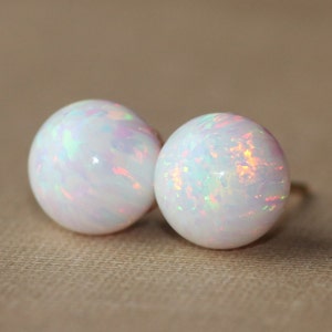 May include: A pair of white opal stud earrings with iridescent rainbow colors.