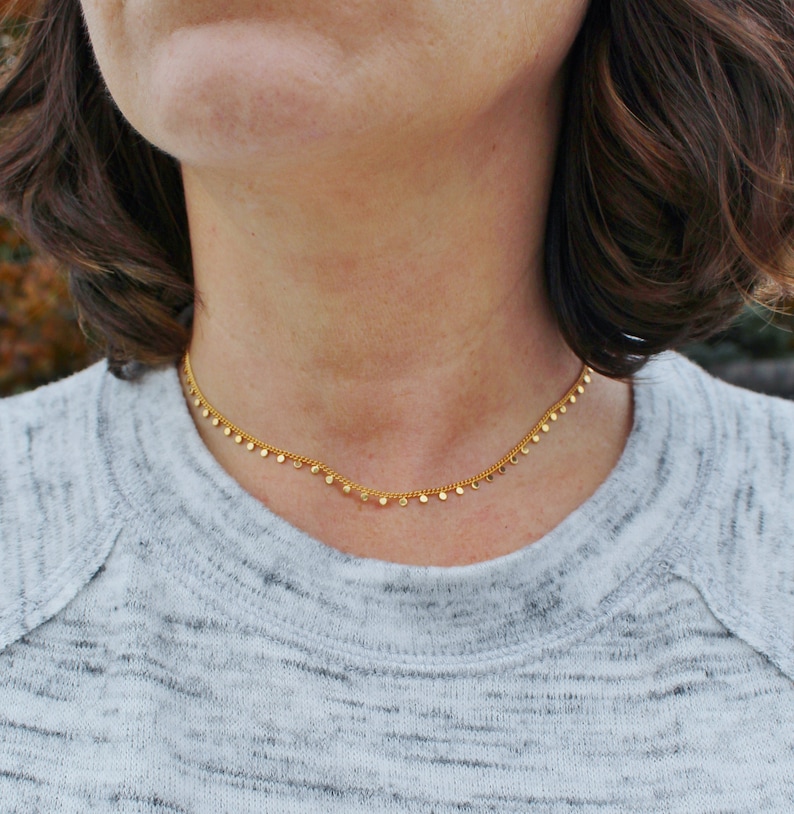 Puede incluir: Un collar de cadena de oro con peque&ntilde;os colgantes redondos. El collar lo lleva una persona con cabello casta&ntilde;o.