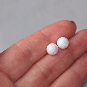 May include: A pair of white opal stud earrings. The earrings are round and have a shimmery, iridescent finish.