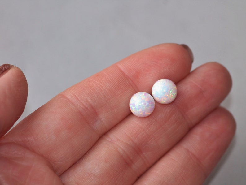 May include: A pair of white opal stud earrings. The earrings are round and have a shimmery, iridescent finish.