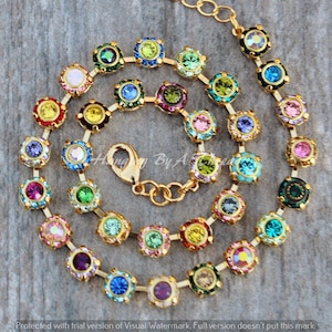 Puede incluir: Un collar de cadena dorada con cierre de broche. La cadena está adornada con pequeñas piedras de cristal redondas y de colores.