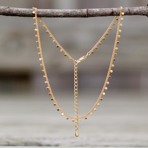 Puede incluir: Un collar de cadena dorada con un delicado colgante de gota y peque&ntilde;os abalorios redondos que cuelgan de la cadena.