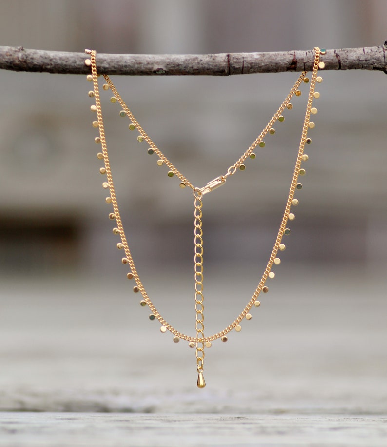 Puede incluir: Un collar de cadena dorada con un delicado colgante de gota y peque&ntilde;os abalorios redondos que cuelgan de la cadena.