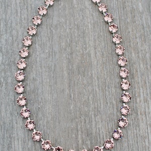 May include: A delicate silver chain necklace with a row of pale pink crystal stones.