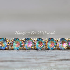 May include: A gold bracelet with iridescent rainbow-colored stones. The bracelet is made of small, round stones that are set in a gold metal setting. The stones are arranged in a row and are connected by a thin gold chain. The bracelet is on a wooden surface.