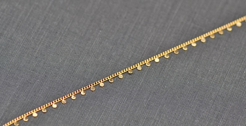 Puede incluir: Un collar de cadena dorada con peque&ntilde;os colgantes redondos.