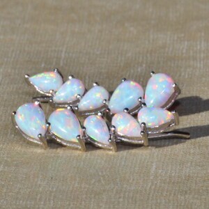 Pu&ograve; includere: Spilla argentata con un gruppo di opali a forma di pera. Gli opali hanno una base bianca latte con lampi iridescenti di colore. La spilla &egrave; progettata per assomigliare a un rametto di foglie.