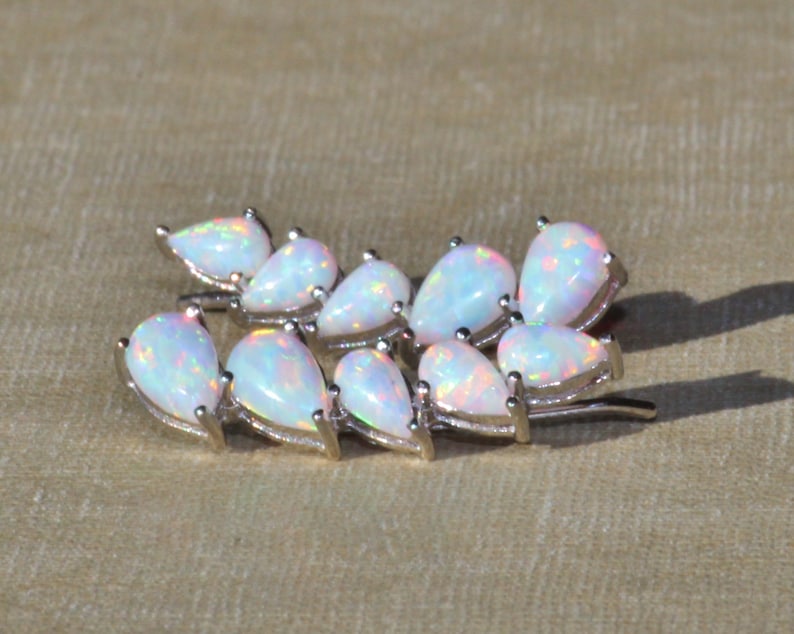 Pu&ograve; includere: Spilla argentata con un gruppo di opali a forma di pera. Gli opali hanno una base bianca latte con lampi iridescenti di colore. La spilla &egrave; progettata per assomigliare a un rametto di foglie.