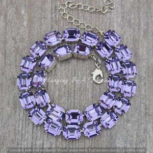 May include: A necklace featuring a series of rectangular, faceted lavender-colored crystals set in silver-toned metal frames. The piece includes a silver-toned chain with a lobster claw clasp and an extender chain for adjustable length.