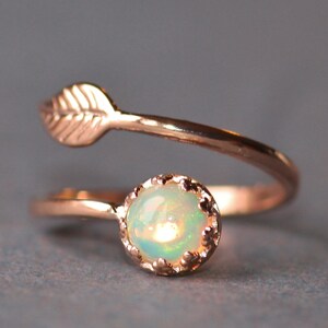 May include: A delicate rose gold ring with a small opal gemstone and a leaf design. The ring is a simple and elegant piece of jewelry.