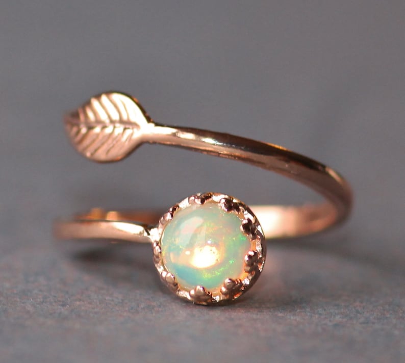 May include: A delicate rose gold ring with a small opal gemstone and a leaf design. The ring is a simple and elegant piece of jewelry.