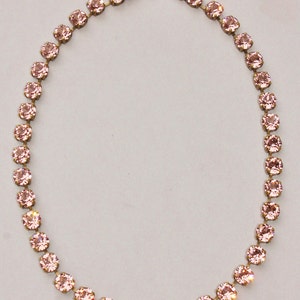 May include: A delicate pink crystal necklace with a gold chain and clasp. The necklace is made of small, round crystals that are strung together in a single row.