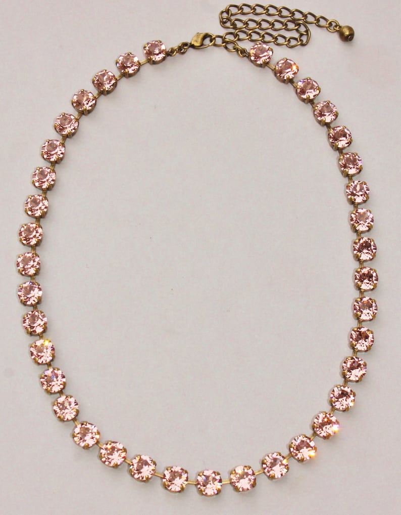 May include: A delicate pink crystal necklace with a gold chain and clasp. The necklace is made of small, round crystals that are strung together in a single row.