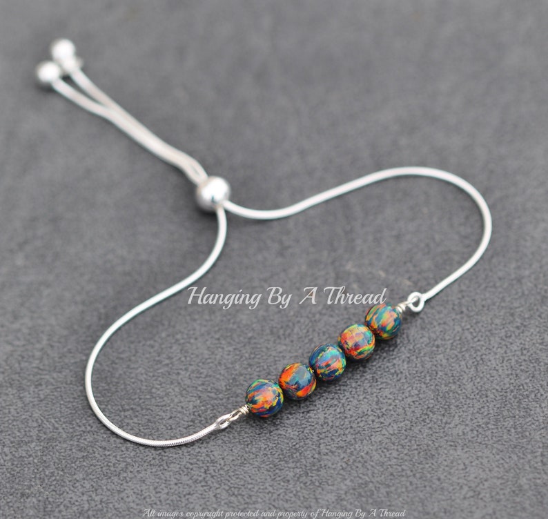 May include: A silver chain bracelet with a sliding clasp and six colorful beads. The beads are a dark blue base with orange, yellow, and green swirls.