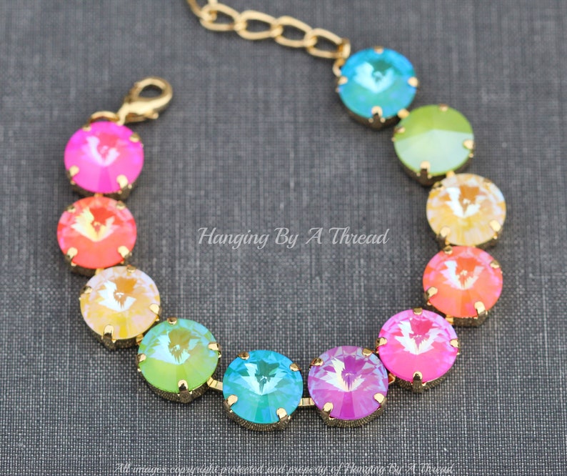 May include: A gold chain bracelet with a rainbow of iridescent crystal beads. The beads are arranged in a gradient from pink to green. The bracelet has a lobster claw clasp.