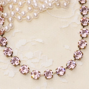 May include: A delicate pink crystal necklace with a silver chain. The necklace is on a white lace background.