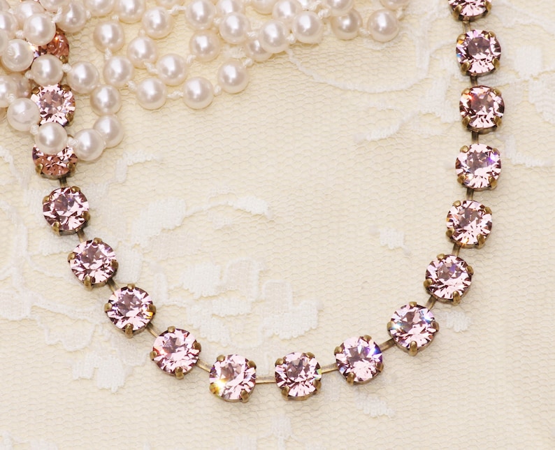 May include: A delicate pink crystal necklace with a silver chain. The necklace is on a white lace background.