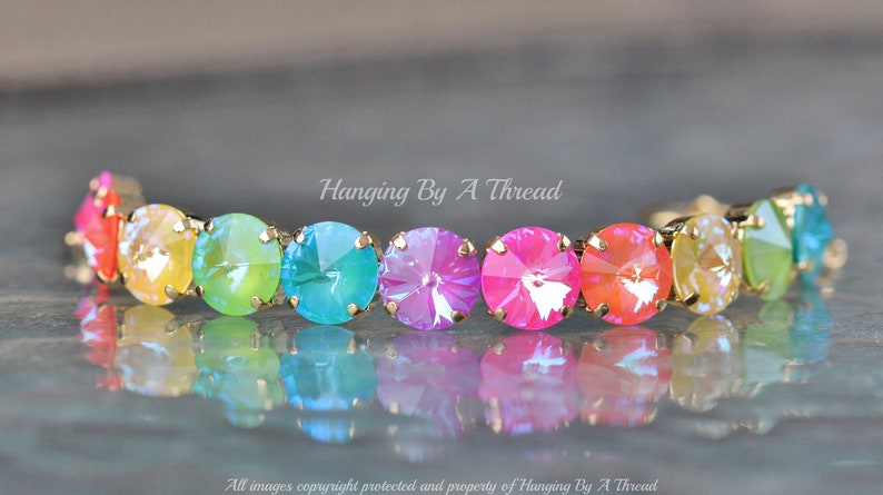 May include: A rainbow-colored crystal bracelet with gold-toned metal accents. The bracelet features a row of round, faceted crystals in shades of red, orange, yellow, green, blue, and purple.