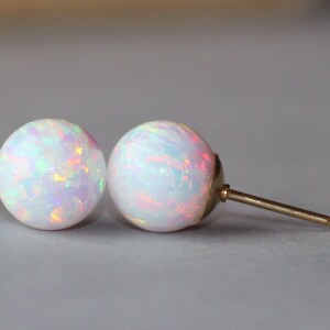 May include: A pair of white opal stud earrings with a gold post.