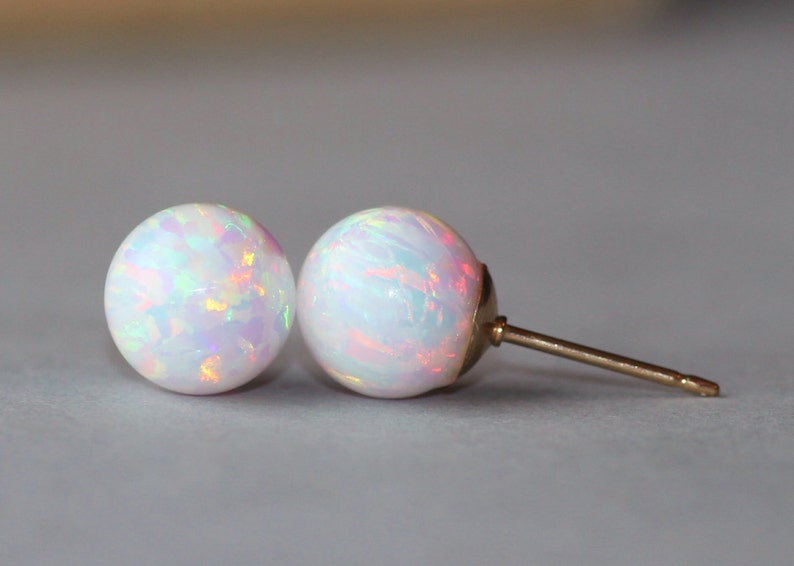 May include: A pair of white opal stud earrings with a gold post.