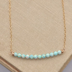 May include: A delicate gold chain necklace with a row of light blue opal beads.