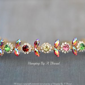 May include: A gold headband with a row of colorful iridescent rhinestones and clear crystals. The headband is decorated with small gold leaves.