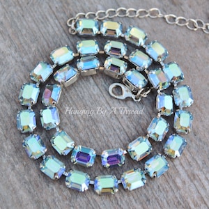 May include: A silver chain necklace with a double row of light blue iridescent rectangular crystals. The necklace has a lobster claw clasp.