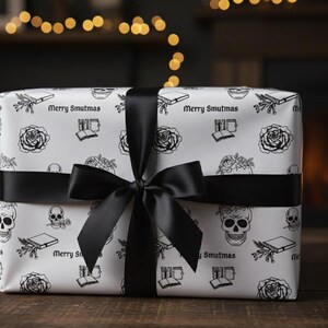 May include: A wrapped gift with white paper featuring black skull, rose, and book illustrations. The paper is tied with a black satin ribbon and bow. The text "Merry Smutmas" is printed on the wrapping paper.