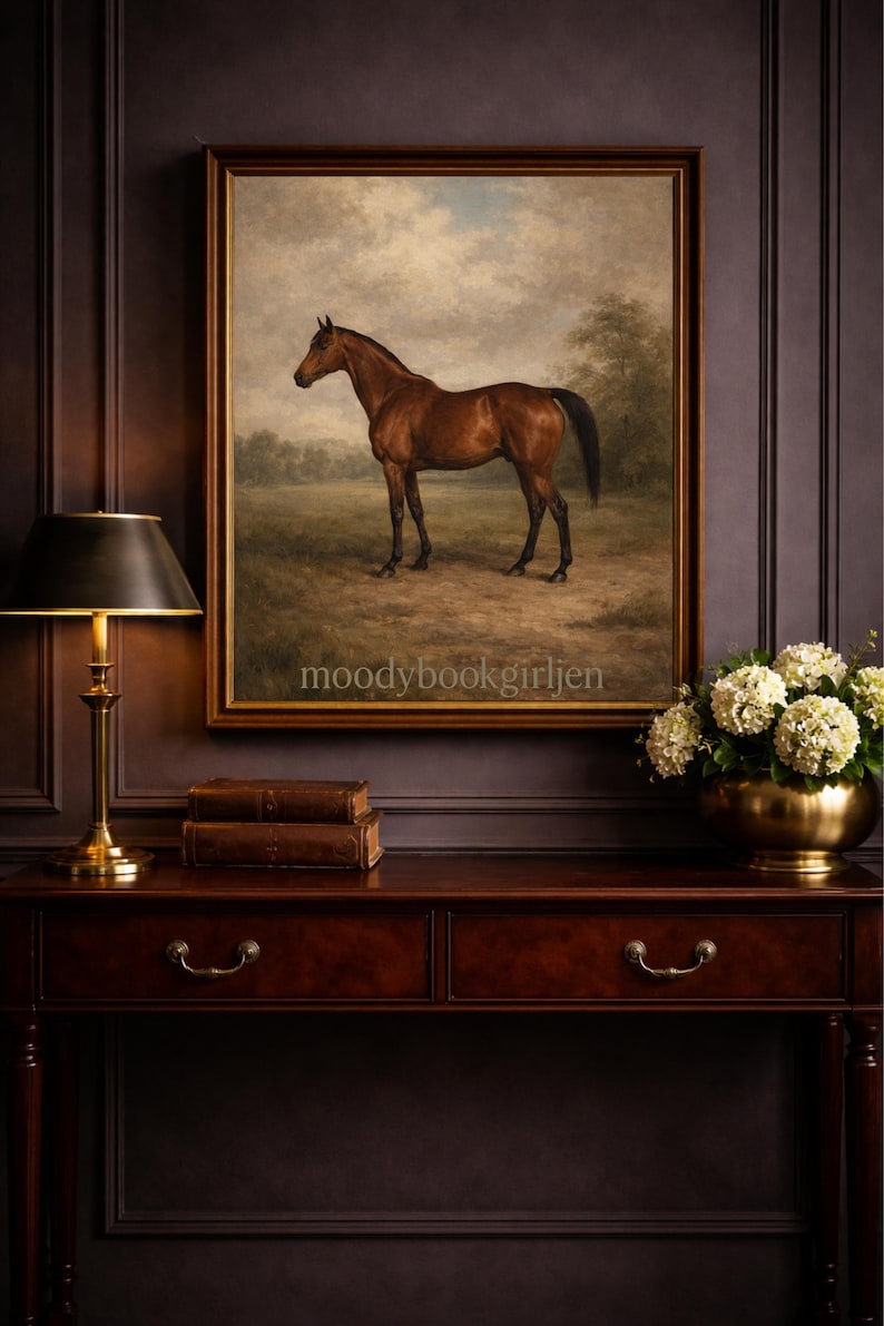 May include: An oil painting of a brown horse in a field, framed and displayed above a dark wood console table. The table has a brass lamp, two leather-bound books, and a gold bowl of white flowers. The wall is a dark brown colour.