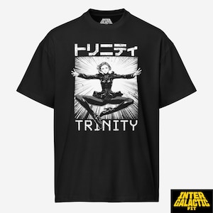 May include: Black t-shirt featuring a graphic of a woman in a dynamic pose, with the word "TRINITY" in white block letters below. Japanese characters are above the image. The shirt has a crew neck and short sleeves.