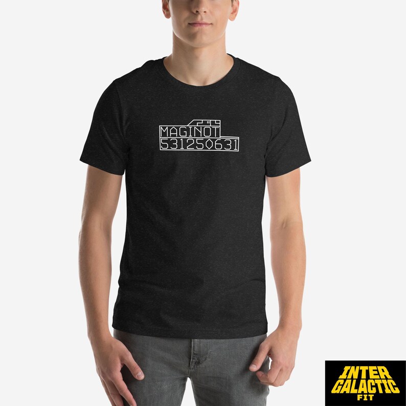 Peut inclure: T-shirt gris fonc&eacute; avec l'inscription blanche "MAGINOT 531250631" imprim&eacute;e sur le devant. Le t-shirt &agrave; manches courtes a un col rond. Le logo Inter Galactic Fit est visible en bas &agrave; droite.