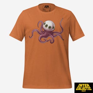 Peut inclure: T-shirt orange avec un dessin d'un poulpe de dessin animé. Le poulpe a une tête blanche, plusieurs yeux verts et des tentacules violets. Le t-shirt porte le texte "INTER GALACTIC FIT" dans un encadré jaune et noir en bas.