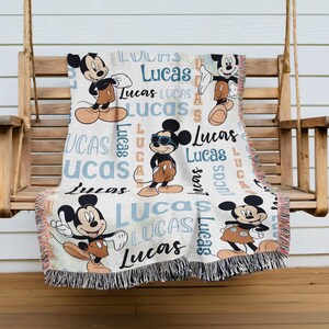 A Mickey Mouse-themed throw blanket with the name "Lucas" printed on it, hanging on a wooden bench.