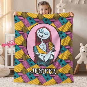A young girl is holding up a colorful blanket featuring a character from the movie "Sally" with the name "Jennifer" printed on it.