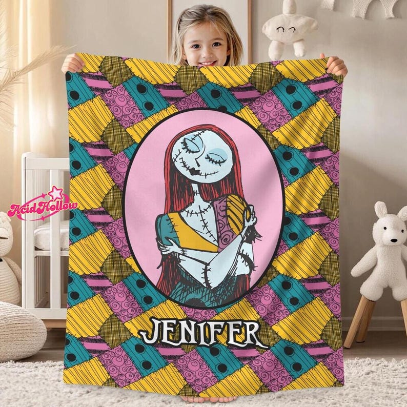 A young girl is holding up a colorful blanket featuring a character from the movie "Sally" with the name "Jennifer" printed on it.