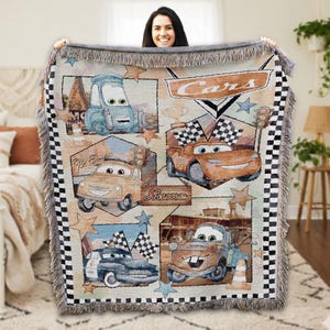 A woman is holding up a colorful blanket featuring various cartoon cars, including the Cars characters from the Disney animated film.