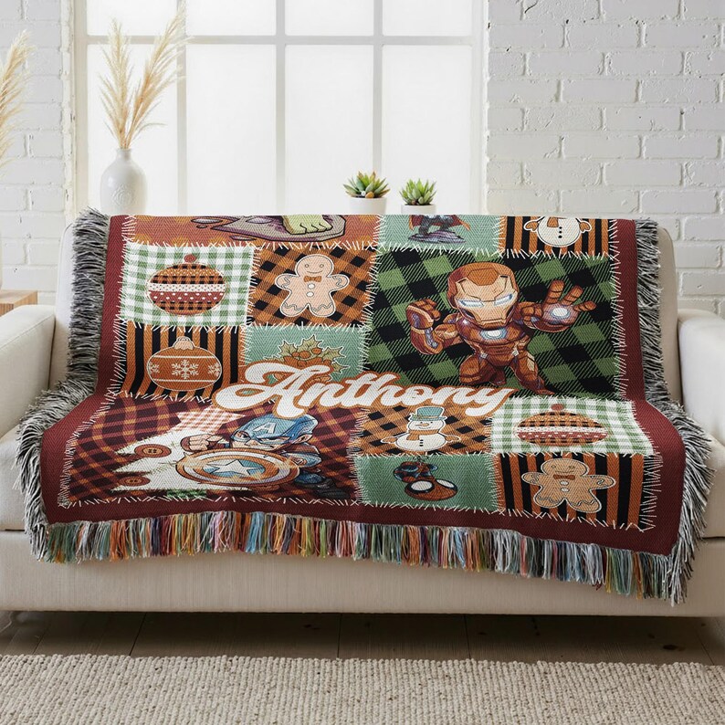 A colorful, patchwork blanket with various cartoon characters and designs, including a character named "Antony" and a gingerbread man. The blanket is placed on a white couch, and there are some decorative elements such as a vase and potted plants in the background.