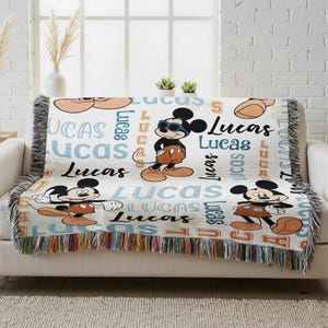 A colorful throw blanket with Mickey Mouse and Lucas characters printed on it, placed on a white couch.