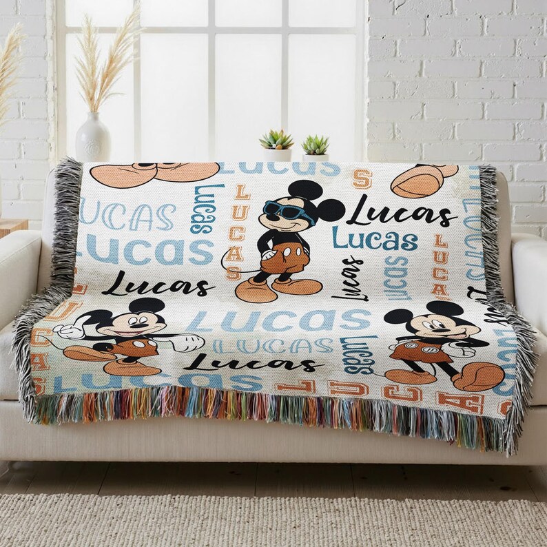 A colorful throw blanket with Mickey Mouse and Lucas characters printed on it, placed on a white couch.
