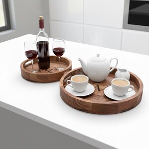 Puede incluir: Dos bandejas de madera. Una contiene una botella de vino tinto y dos copas de vino. La otra tiene una tetera blanca, dos tazas de caf&eacute; y una jarrita de crema. Las bandejas est&aacute;n sobre una superficie blanca.