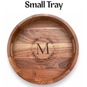 Puede incluir: Una bandeja redonda de madera con un acabado de vetas naturales. La bandeja tiene un borde elevado y dos asas. El centro presenta una corona decorativa alrededor de la letra "M". El texto "Small Tray" est&aacute; en la parte superior.