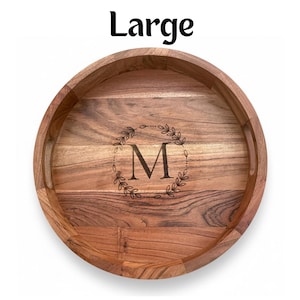 Puede incluir: Una bandeja de madera grande y redonda con un acabado de vetas de madera natural. La bandeja presenta un dise&ntilde;o de corona decorativa alrededor de la letra "M" en el centro. La palabra "Large" est&aacute; impresa en negro en la parte superior.
