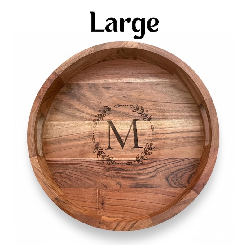 Puede incluir: Una bandeja de madera grande y redonda con un acabado de vetas de madera natural. La bandeja presenta un dise&ntilde;o de corona decorativa alrededor de la letra "M" en el centro. La palabra "Large" est&aacute; impresa en negro en la parte superior.