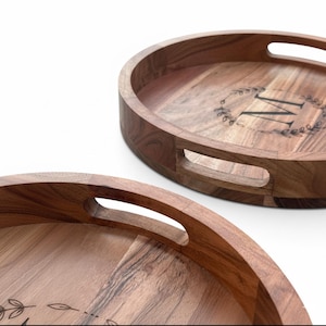 Puede incluir: Dos bandejas ovaladas de madera con un acabado de vetas naturales. Cada bandeja tiene un recorte para el asa y una inicial decorativa "M" dentro de una corona. Las bandejas son adecuadas para servir alimentos o exhibir art&iacute;culos. Aproximadamente 30 cm de di&aacute;metro.