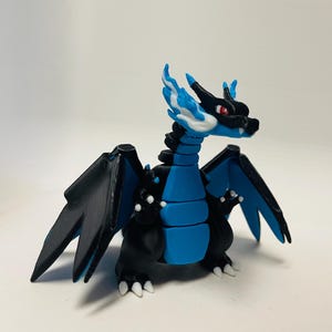 May include: A 3D-printed figurine of a dragon-like creature. The figure is primarily black and blue, with white accents on the claws and flames. The dragon has large wings and a detailed design, with red eyes.